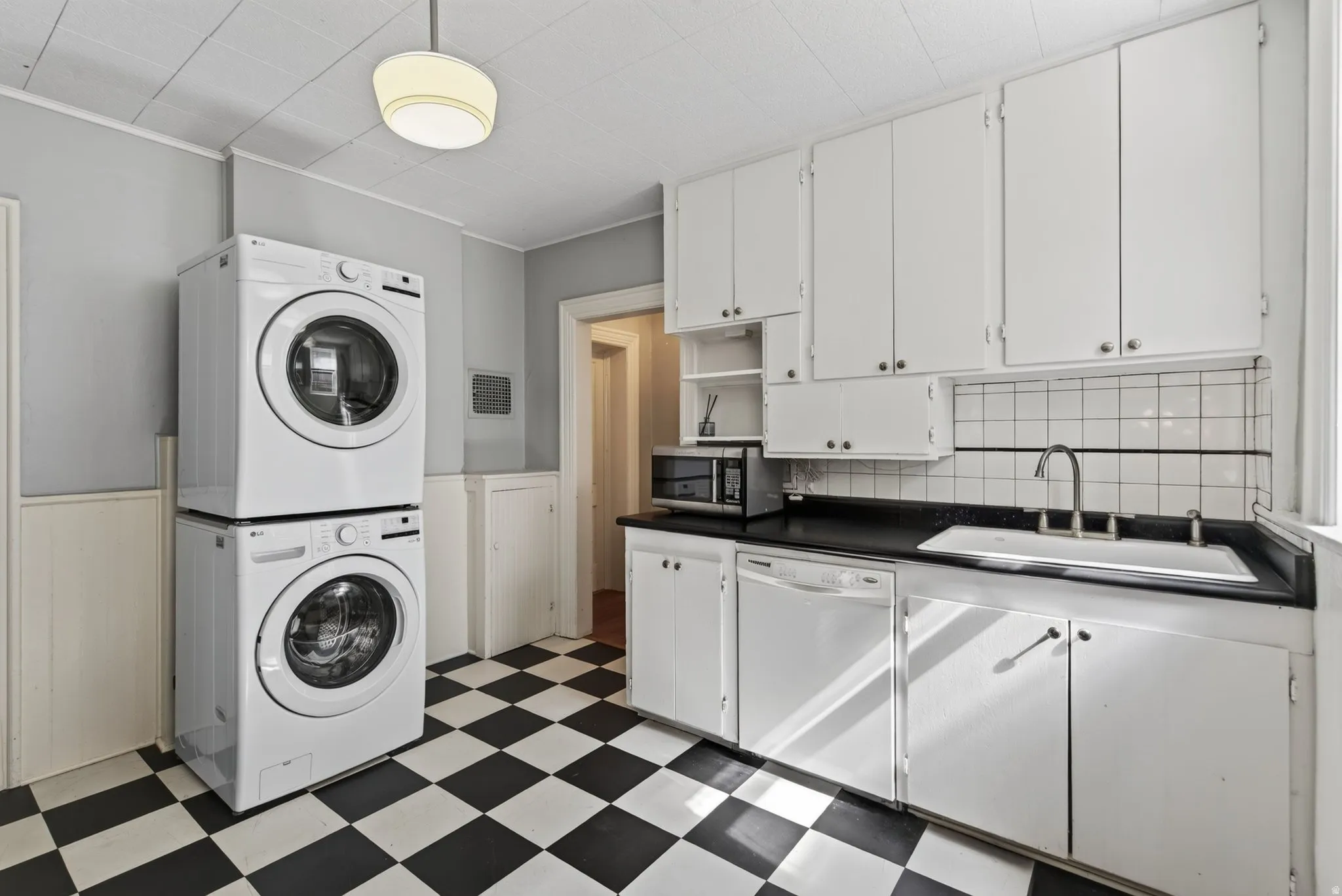 Kitchen area featuring stacked white washer and dryer, checkerboard flooring, white cabinetry, dark countertops, and a white tiled backsplash