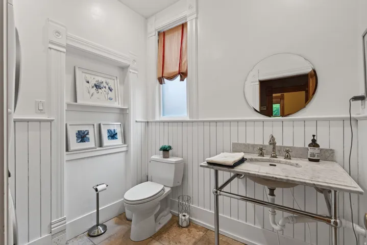 Bathroom featuring wainscoting, an integrated sink with a stone countertop, and a wall-mounted mirror