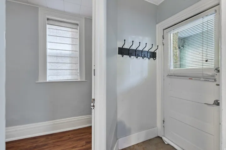 Entryway featuring a white paneled door with integrated blinds, a wall-mounted coat rack, light gray walls, and white trim