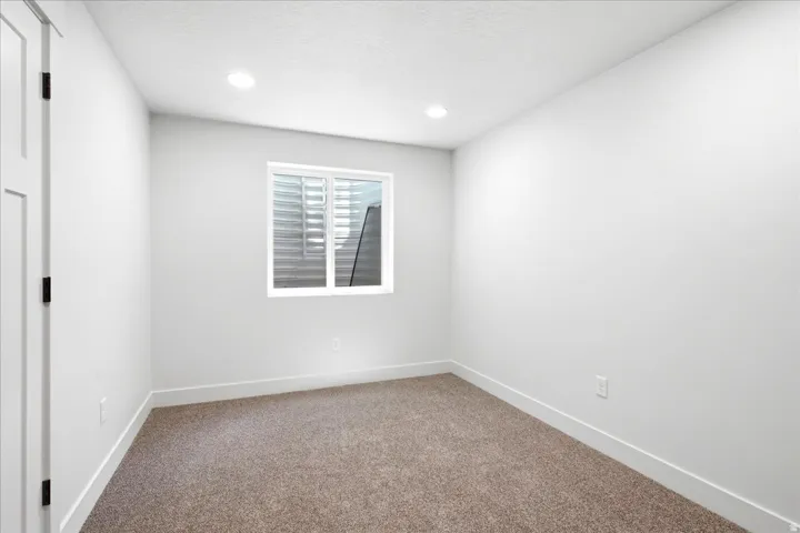 Bright room featuring a window with integrated blinds, recessed lighting, white walls, white trim, and brown carpet flooring