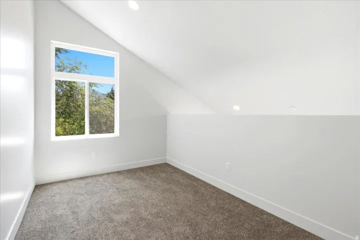 Vaulted ceiling room featuring a large window, recessed lighting, and neutral carpeting