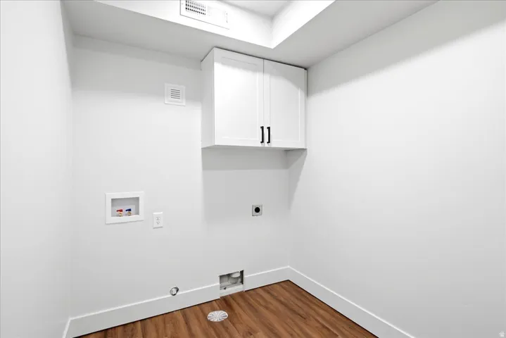 Dedicated laundry space featuring wood-finish flooring, white walls, and built-in white cabinetry with black hardware