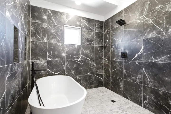 Freestanding soaking tub within a curbless shower area, featuring dark veined tile walls and a square rain showerhead