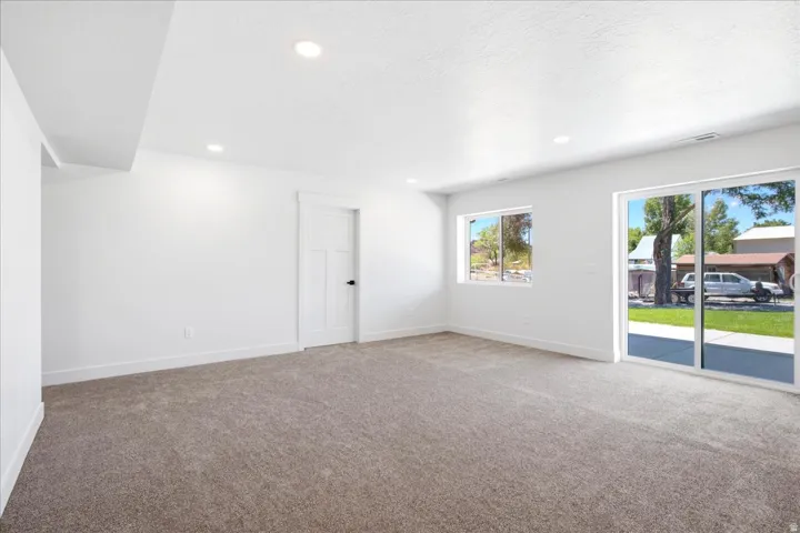 Spacious room featuring neutral carpeting, white walls, recessed lighting, and a white interior door