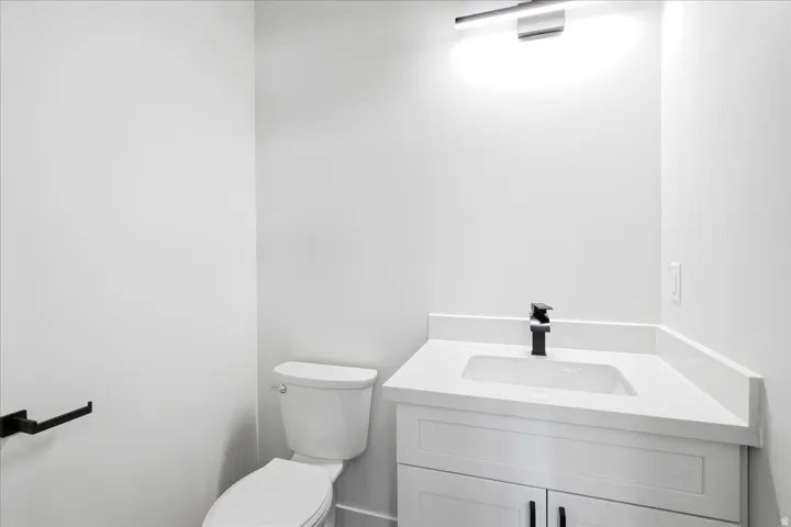 Contemporary powder room featuring a white single-sink vanity with a solid surface countertop, matte black faucet, and white shaker-style cabinetry with matte black hardware