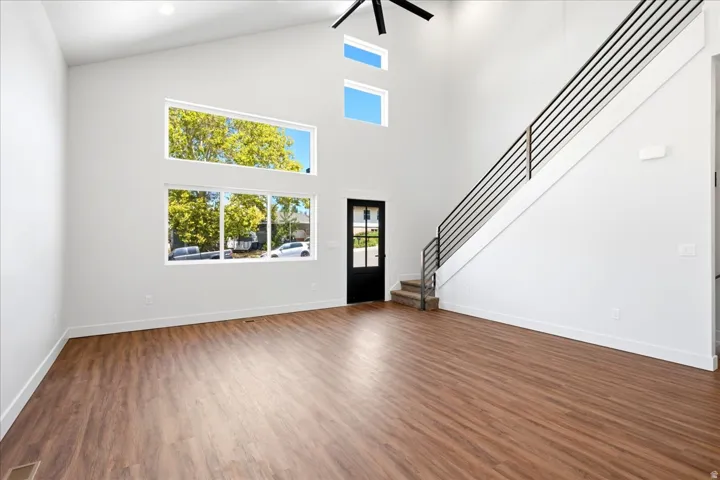 Spacious main living area featuring soaring vaulted ceilings, wood-finish flooring, and a contemporary open-riser staircase with horizontal metal railing