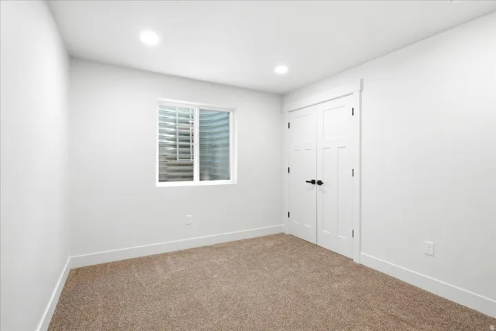 Room featuring neutral carpet flooring, white walls, and a white window with a window well