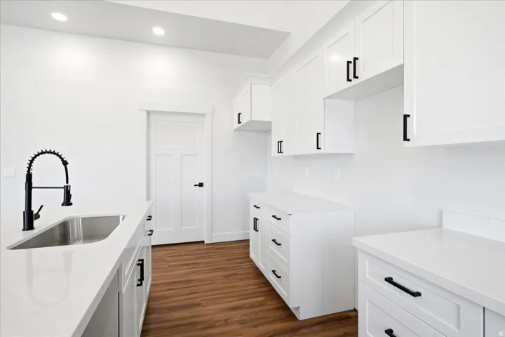 Modern kitchen featuring white cabinetry with black hardware, white countertops, a stainless steel undermount sink with a matte black faucet, wood-finish flooring, and recessed lighting