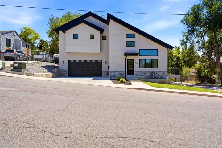 Contemporary facade featuring a light-colored stucco exterior, a dark-colored sloped roof, and a stone veneer foundation