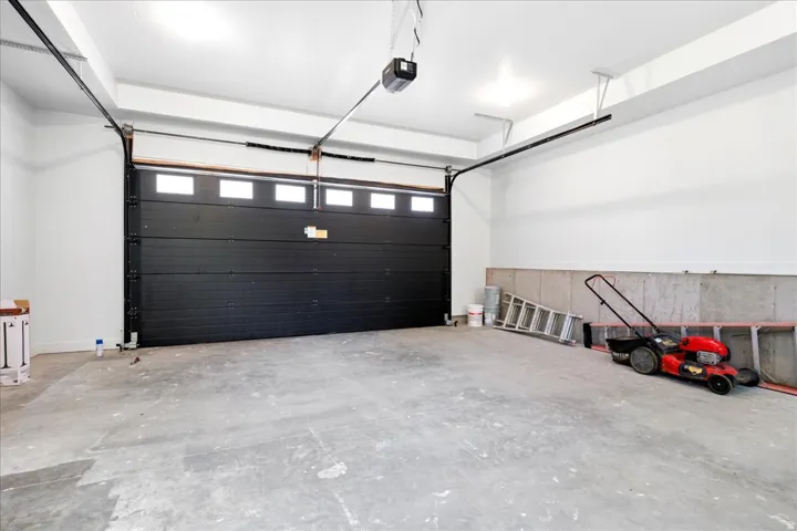 Spacious garage featuring a black sectional garage door with transom windows, a smooth concrete floor, and white painted walls
