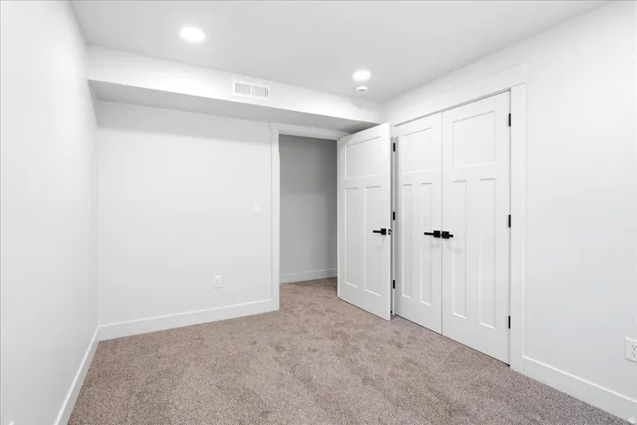 Carpeted room featuring white walls, contemporary white paneled doors with black hardware, recessed lighting, and white trim