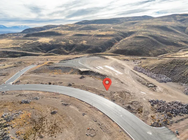 Expansive undeveloped land featuring a cleared building site, established paved roads, and distant mountain scenery