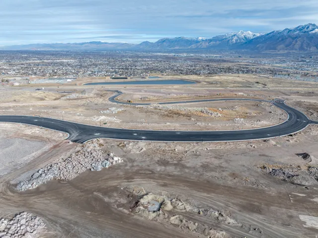 Paved roadways within a developing subdivision, featuring a distant city backdrop and snow-capped mountains