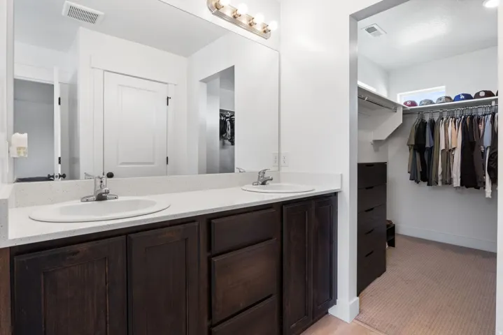 Bathroom vanity with dual undermount sinks, light-toned countertop, and dark wood-finish cabinetry