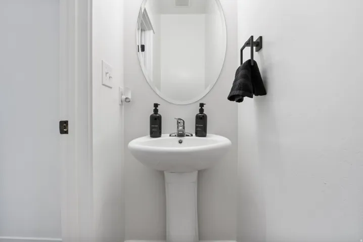 White pedestal sink with a chrome faucet, oval mirror, and matte black towel rack
