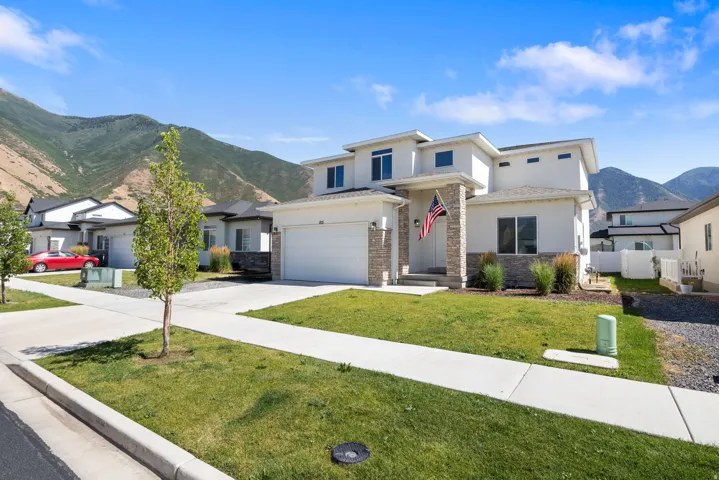 Modern multi-level residence featuring a stucco exterior with stone veneer accents, a prominent two-car garage, and a concrete driveway