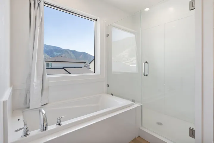 Soaking tub with chrome fixtures beneath a large window, complemented by a glass-enclosed shower with a contemporary handle