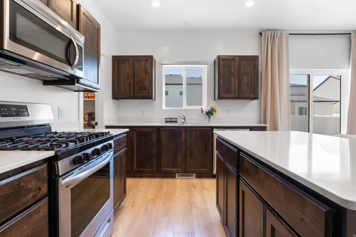 Kitchen featuring stainless steel appliances, wood-finish cabinetry, light-toned countertops, and light wood-finish flooring