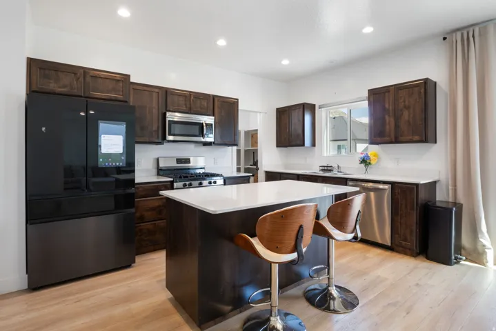 Kitchen featuring dark wood cabinetry, white countertops, stainless steel appliances, and light wood-finish flooring