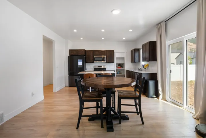 Open-concept kitchen and dining area featuring light wood-finish flooring, dark wood cabinetry, stainless steel appliances, recessed lighting, and a sliding glass door