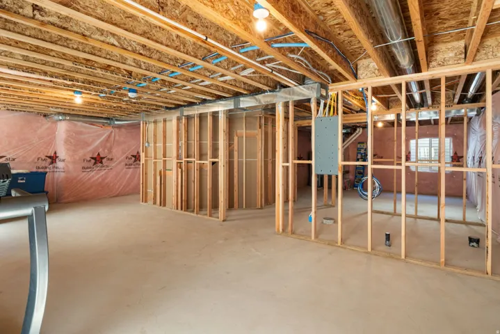 Unfinished basement featuring exposed wood joists, framed interior walls, and a concrete floor