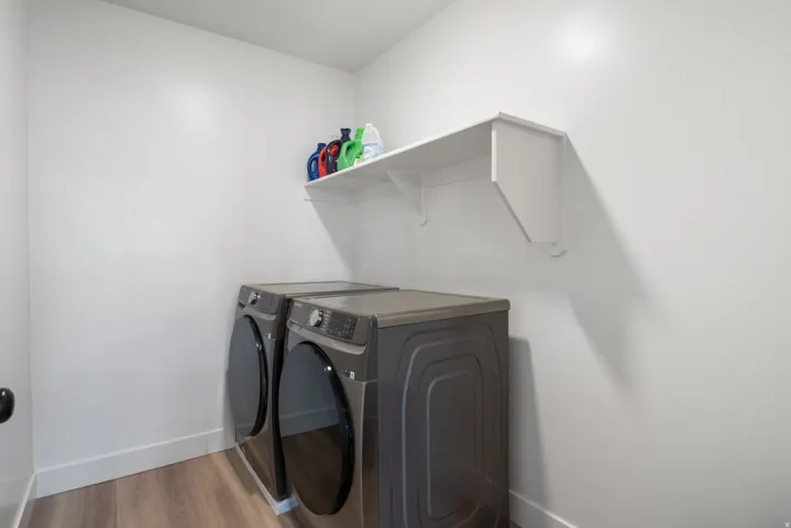 Dedicated laundry area featuring wood-finish flooring, white walls, and a built-in white shelving unit