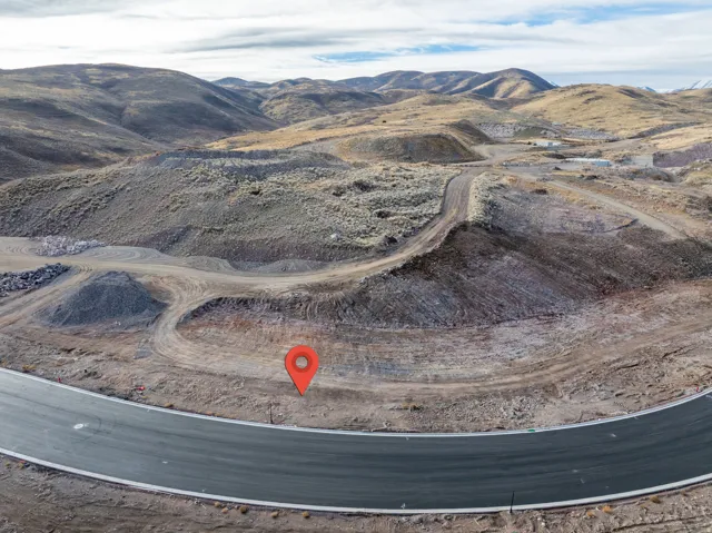 Paved road frontage with a graded lot, surrounded by natural mountainous terrain