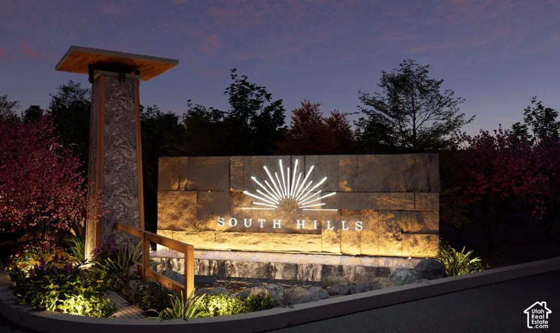 Stone entrance monument featuring illuminated signage, wood-capped stone pillar, and integrated landscape lighting