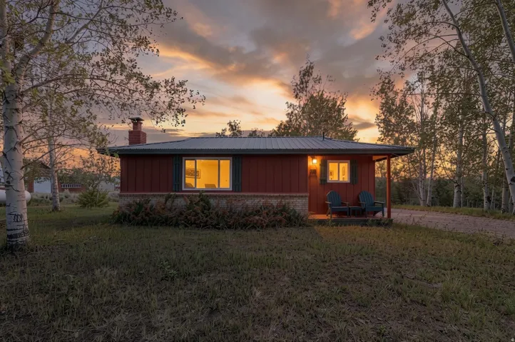 Red-sided home featuring a stone foundation, covered front porch, and metal roof