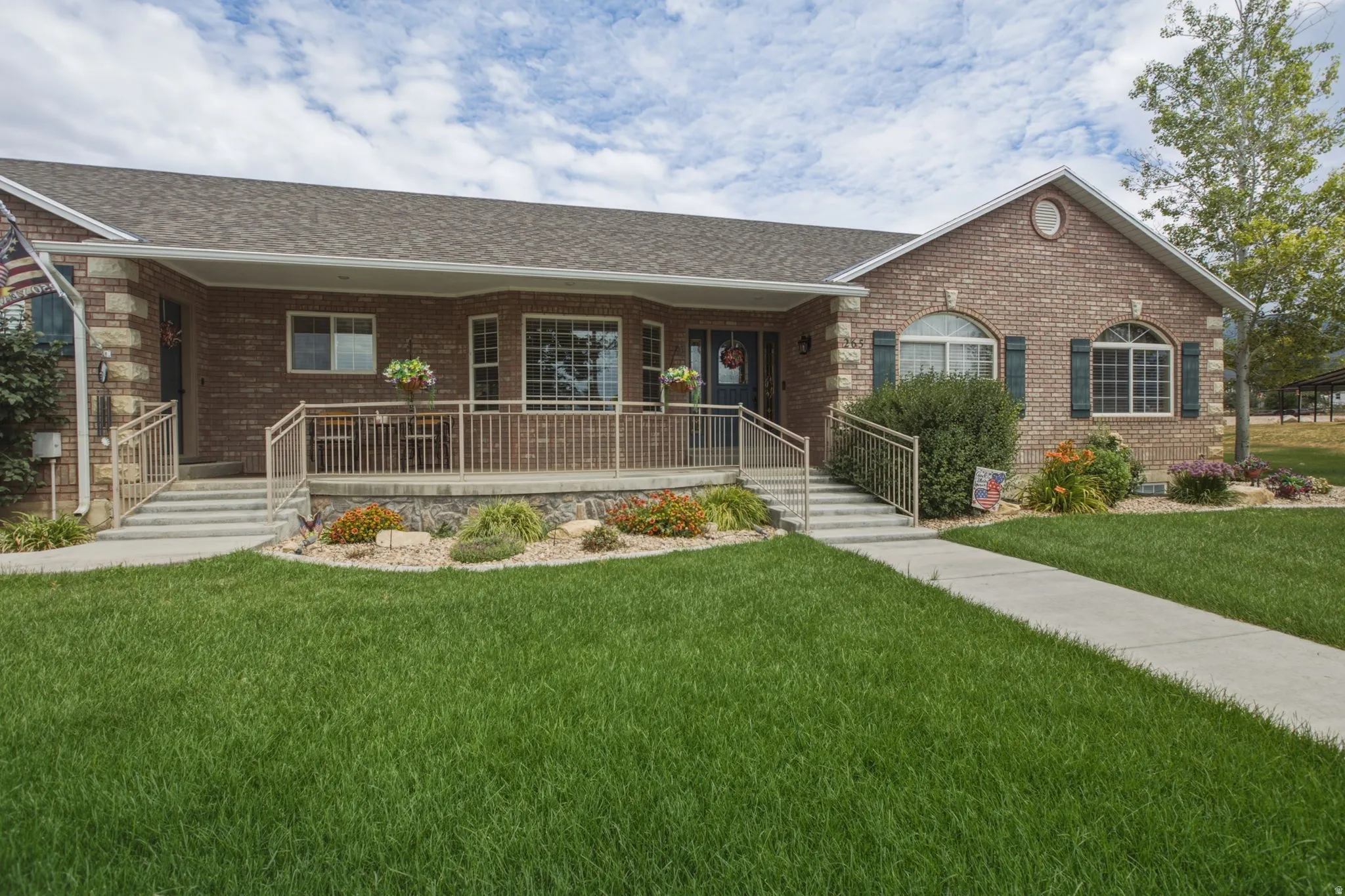 Brick exterior featuring a covered porch with railings, mature landscaping, and an arched window