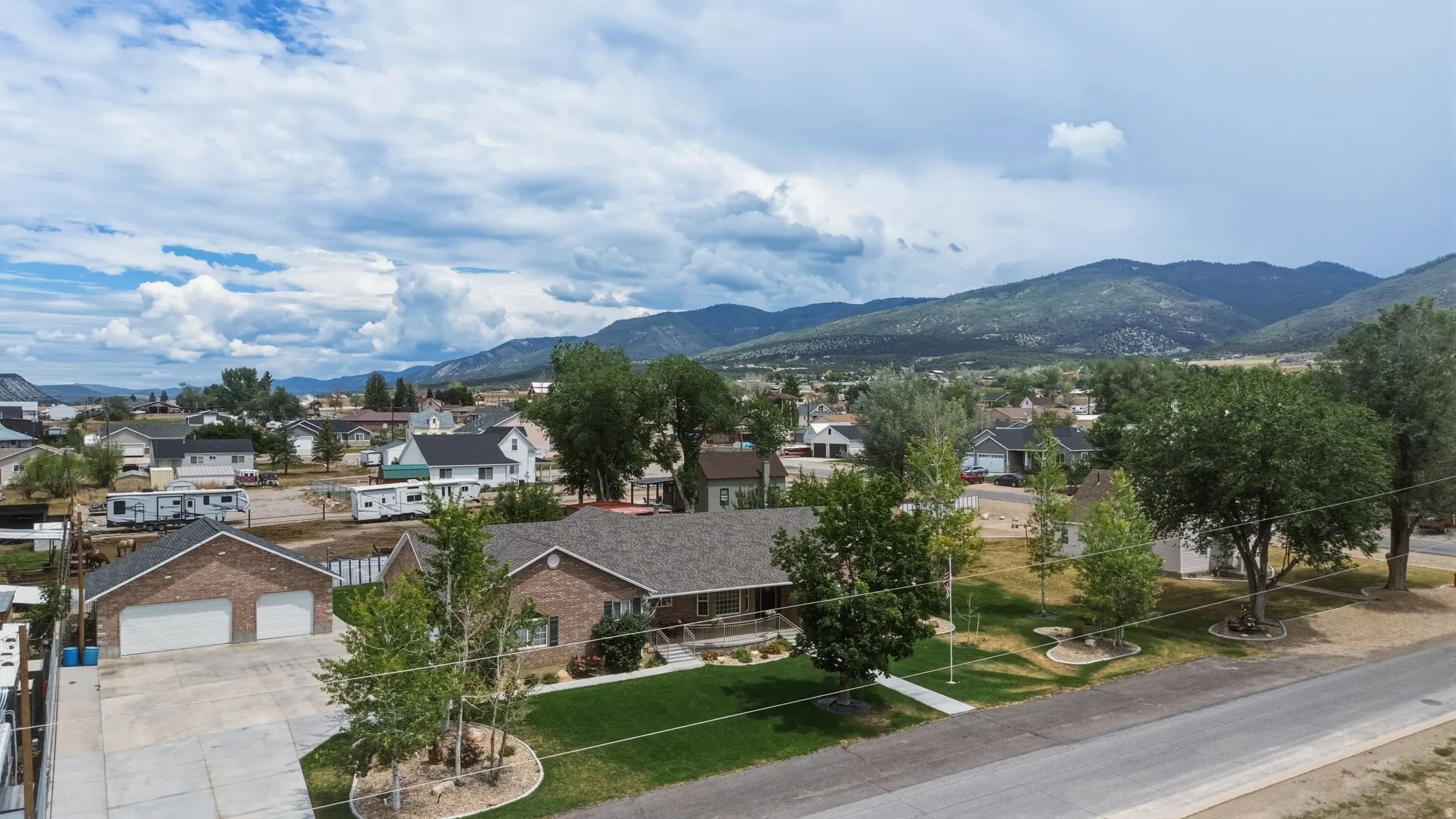 Brick exterior featuring a multi-car garage, mature landscaping, and a mountain backdrop