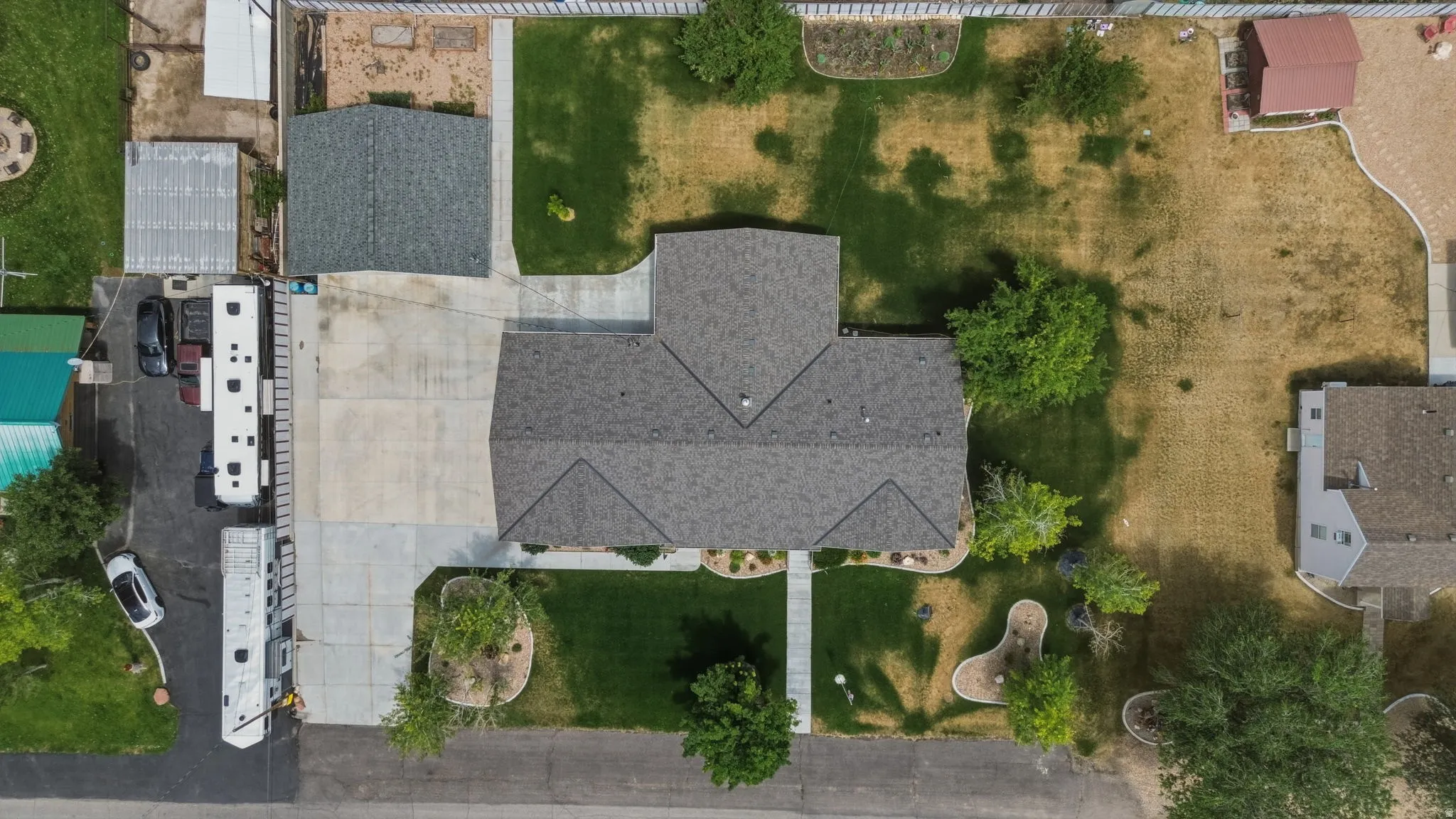 Expansive property featuring a grey shingle roof, a generously sized concrete driveway, and established landscaping