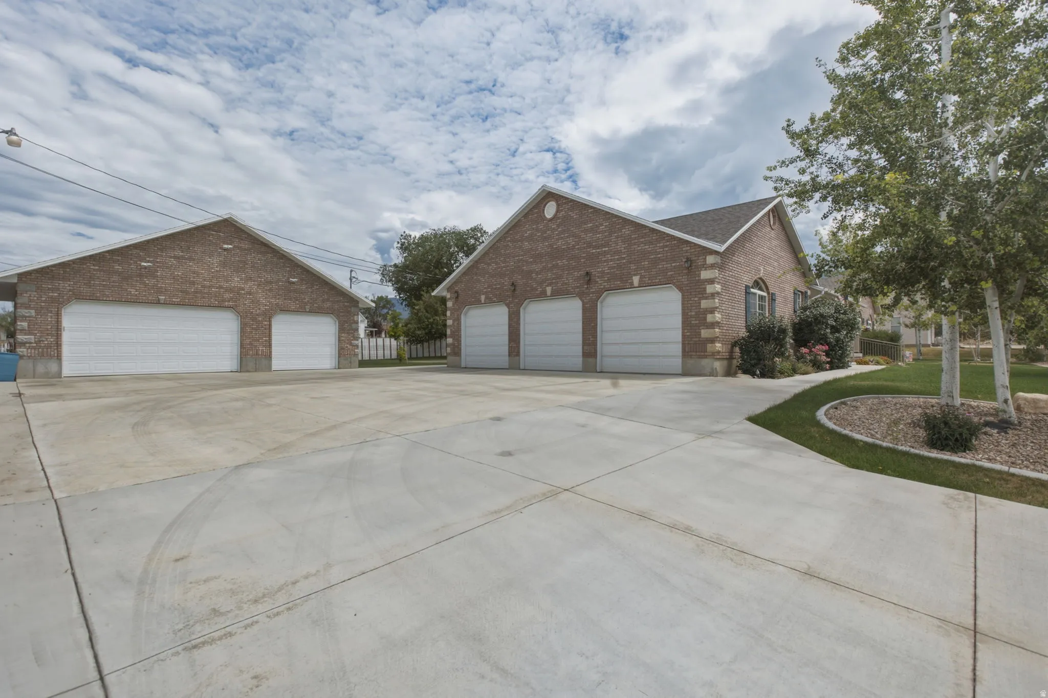 Expansive concrete driveway featuring a main residence with a three-car garage and a detached structure with a two-car garage