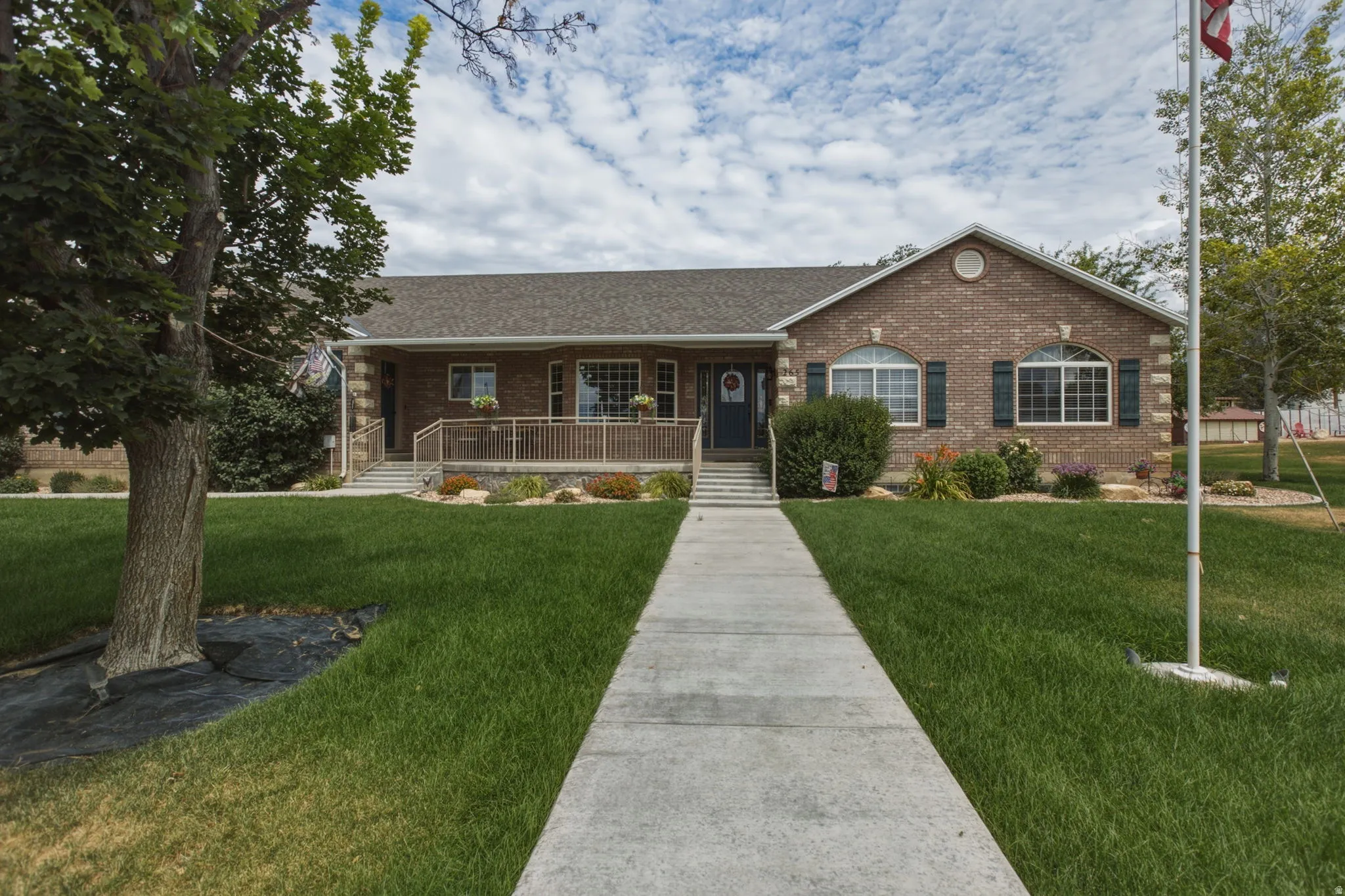 Brick ranch-style residence featuring a prominent front walkway, a covered porch with railing, an arched window, and mature landscaping