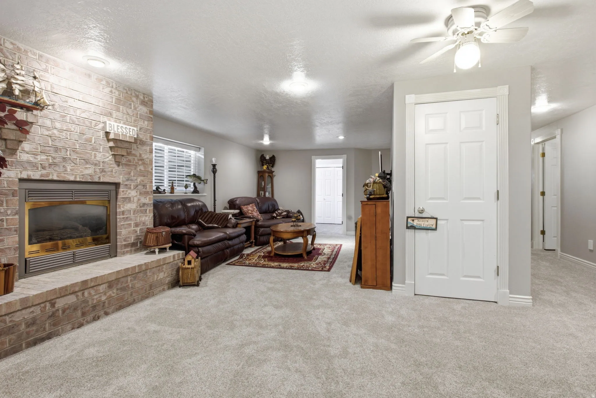 Carpeted living space featuring a brick fireplace with a raised hearth, recessed lighting, a ceiling fan with light fixture, and white interior doors
