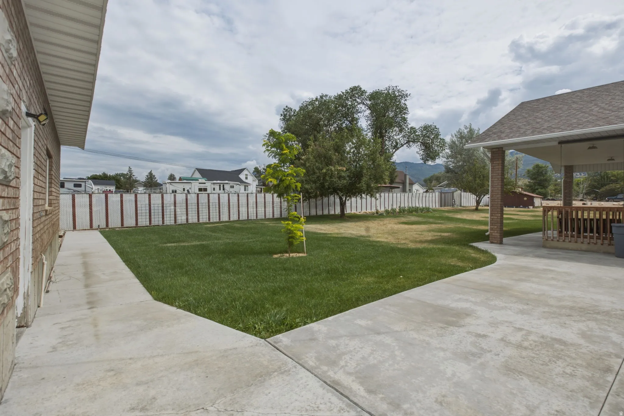 Expansive backyard featuring a concrete patio, a manicured lawn, established trees, and a privacy fence