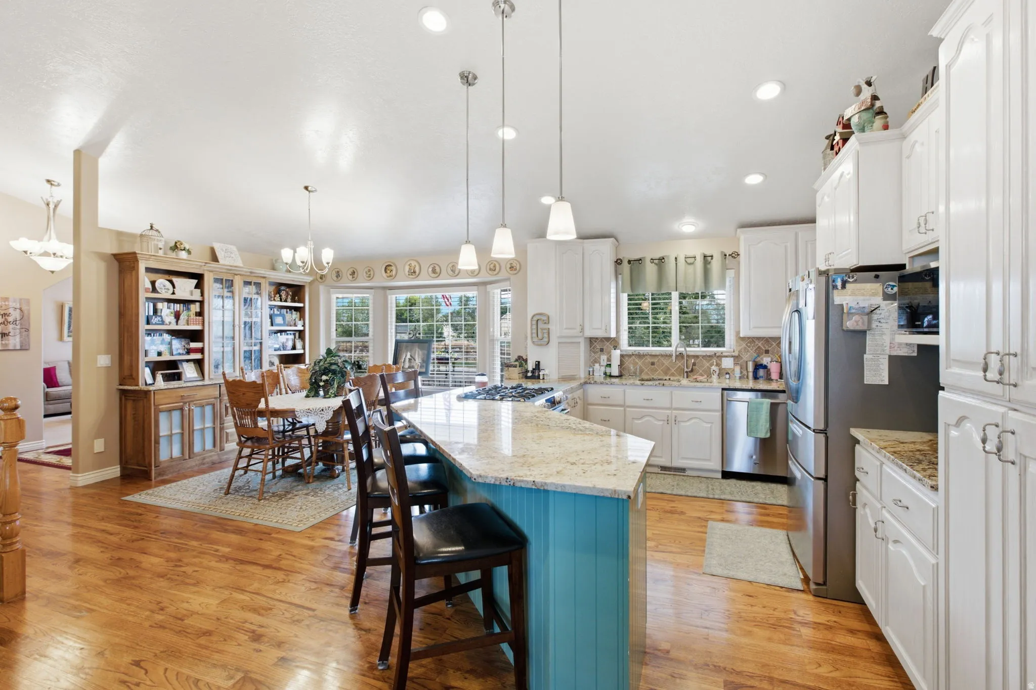 Open-concept kitchen and dining area featuring wood-finish flooring, a vibrant blue kitchen island with a light-colored countertop, white cabinetry, and stainless steel appliances