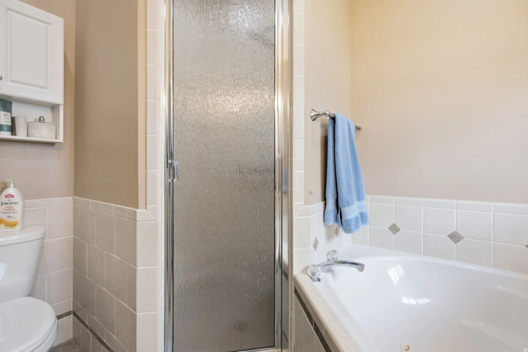 Bathroom featuring a built-in tub with chrome fixtures, a clear glass shower enclosure with chrome frame, and tile wainscoting