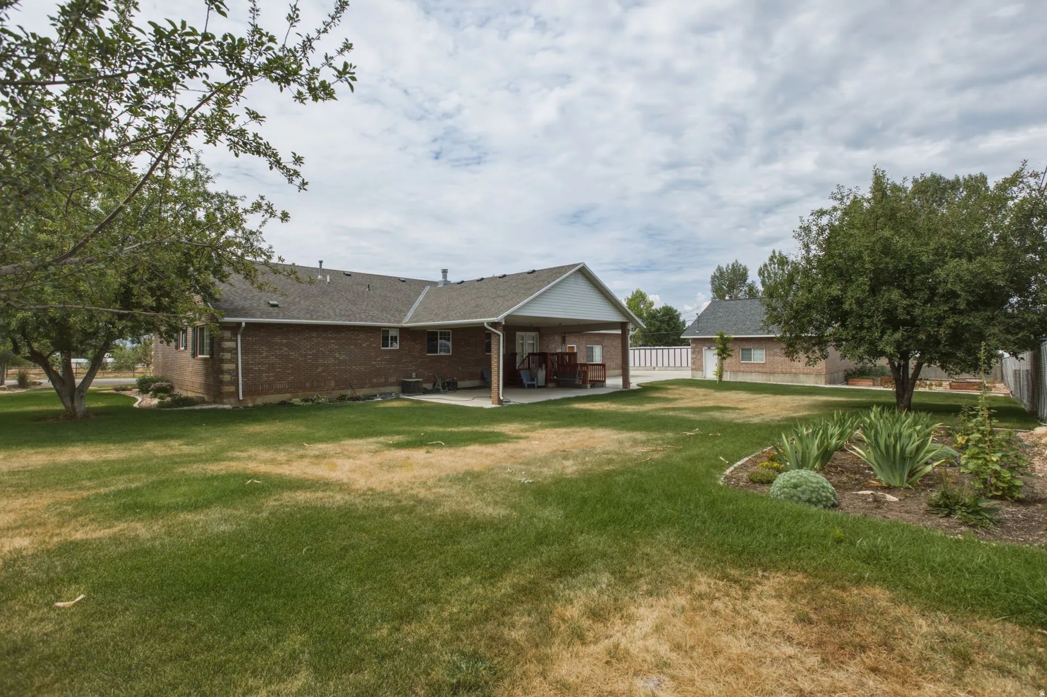 Expansive backyard featuring a brick exterior, covered patio, mature trees, and a separate structure with a shingled roof
