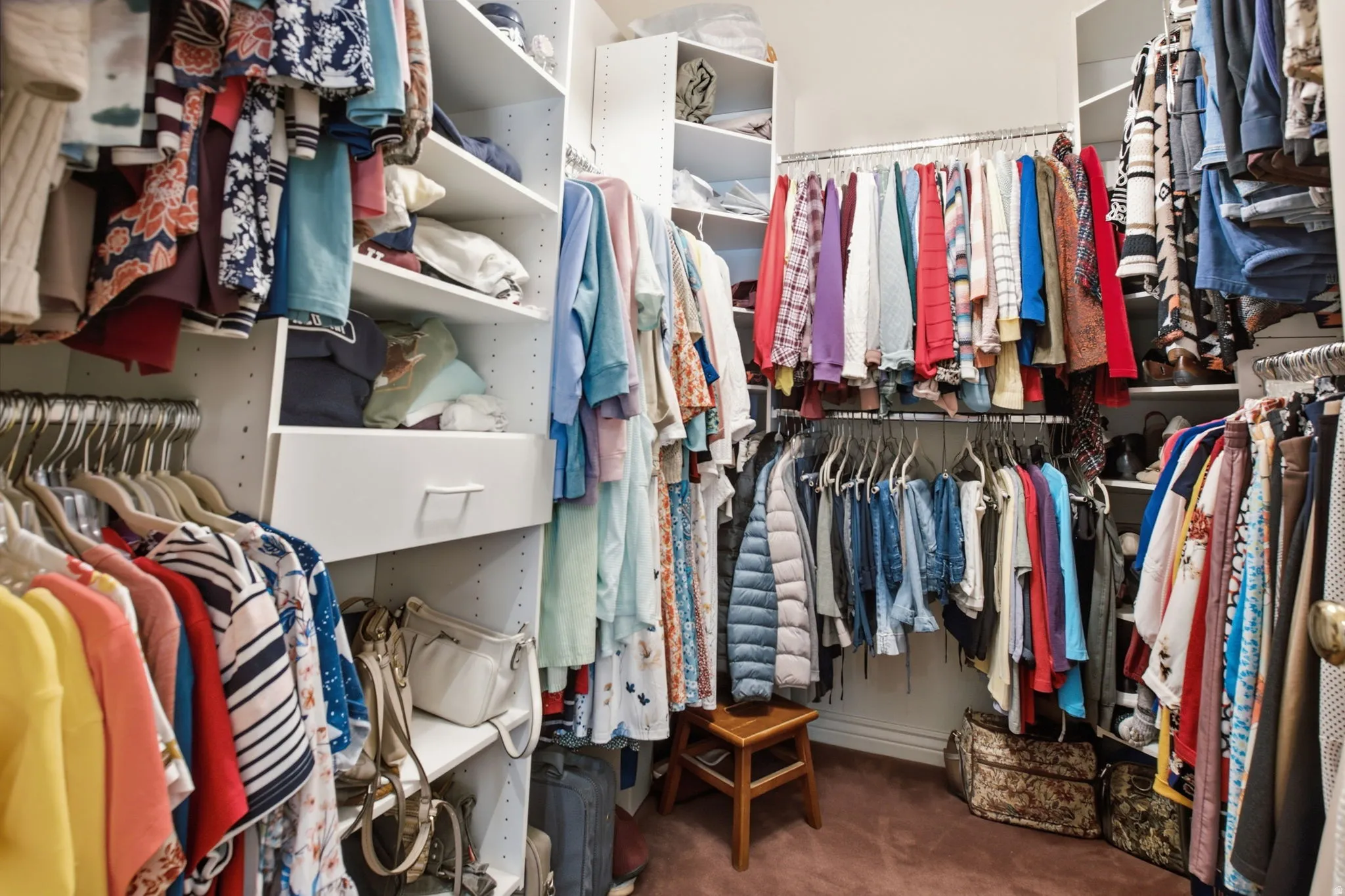 Walk-in closet featuring built-in shelving, multiple hanging rods, corner shelving, and a built-in drawer