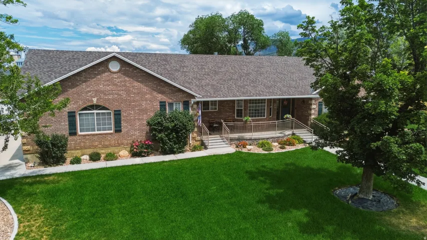 Brick façade residence featuring a covered porch with railings, mature front yard trees, and a well-maintained lawn