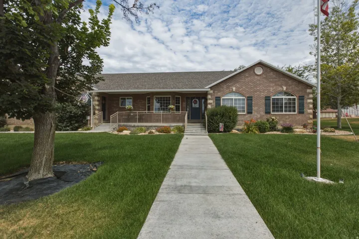 Brick ranch-style residence featuring a prominent front walkway, a covered porch with railing, an arched window, and mature landscaping