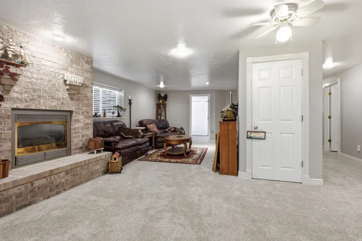 Carpeted living space featuring a brick fireplace with a raised hearth, recessed lighting, a ceiling fan with light fixture, and white interior doors