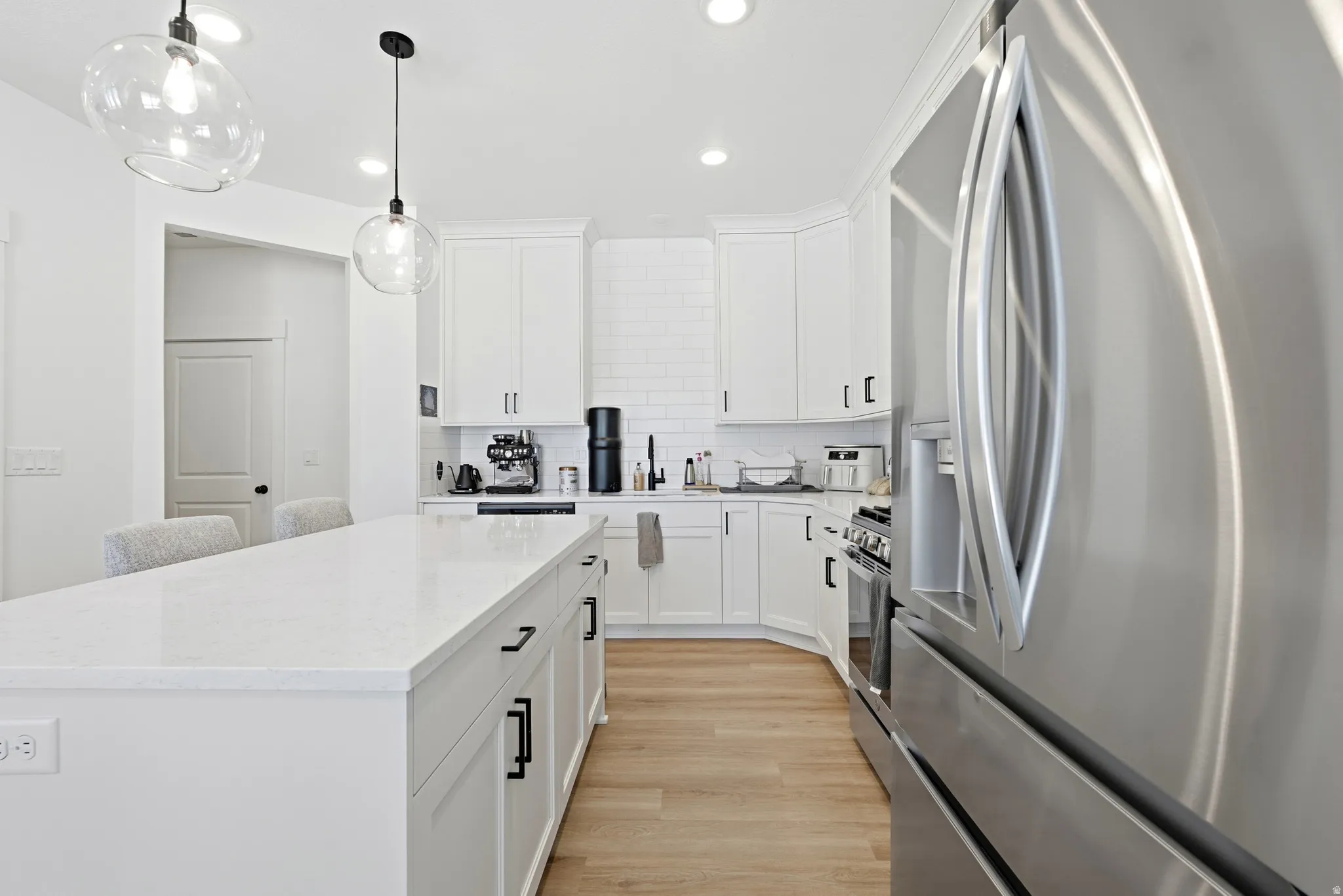 Modern kitchen featuring a large center island with a white countertop, white cabinetry, stainless steel appliances, and wood-finish flooring