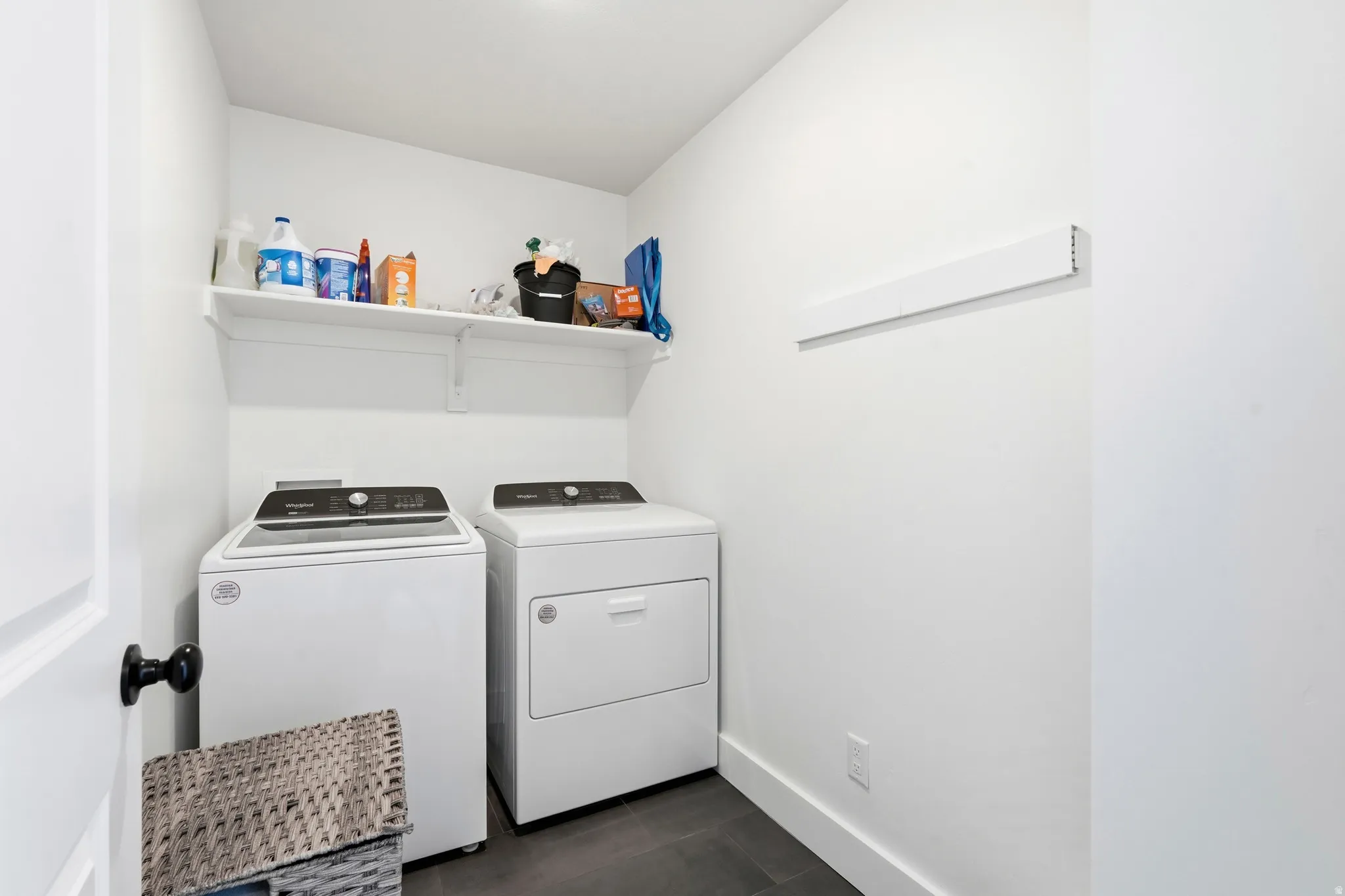 Dedicated laundry space featuring a white washer and dryer set, dark tile flooring, and an elevated storage shelf