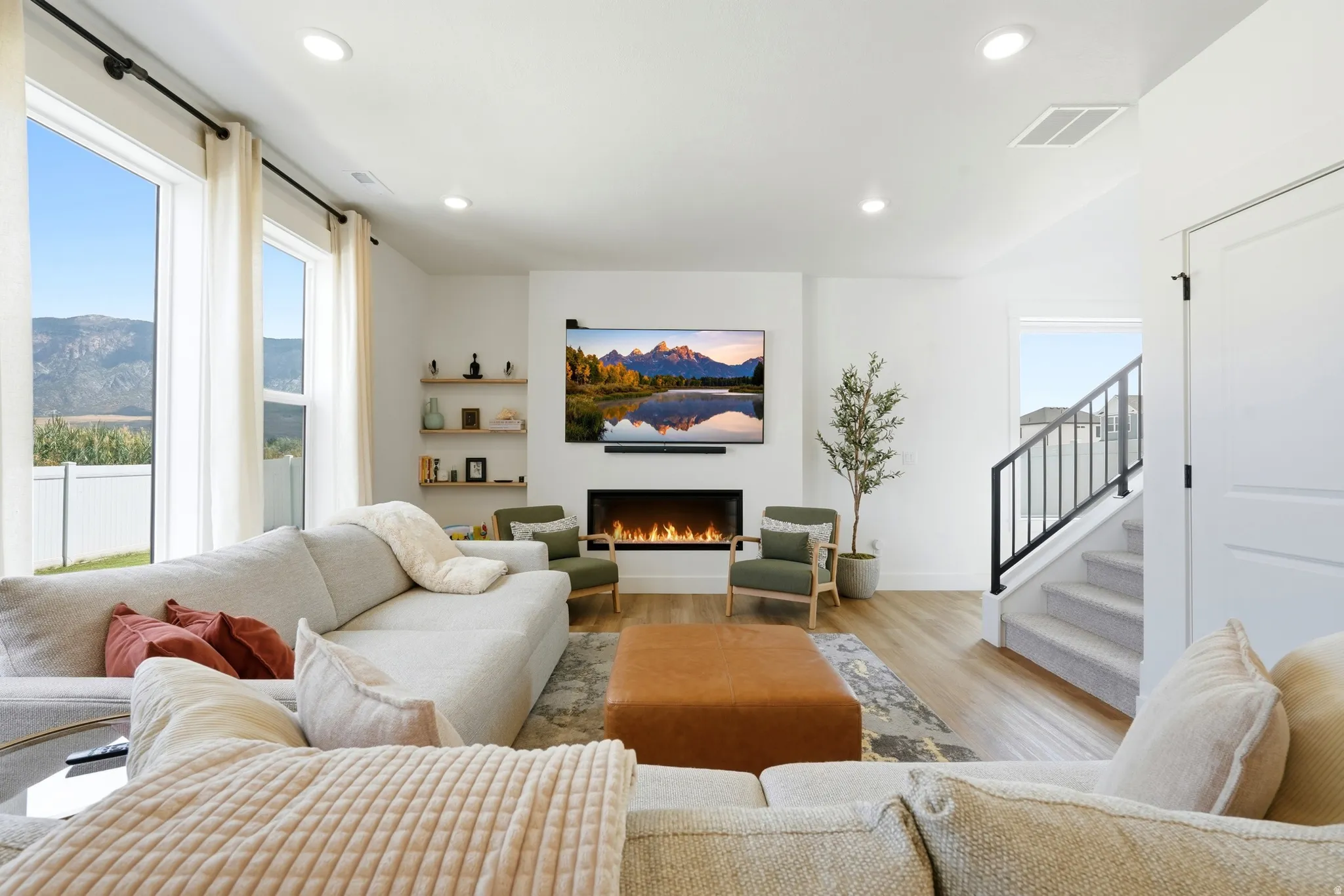 Spacious living area featuring large windows, wood-finish flooring, a contemporary fireplace, recessed lighting, and built-in shelving