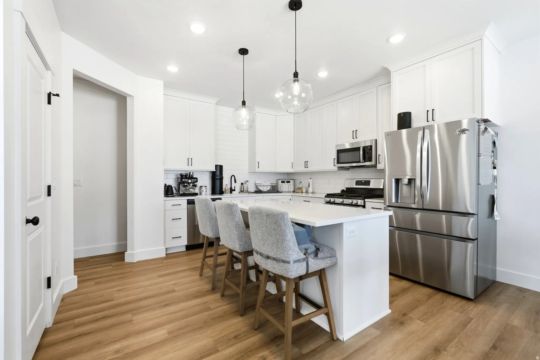 Modern kitchen featuring white cabinetry, stainless steel appliances, an island with seating, pendant lighting, and wood-finish flooring