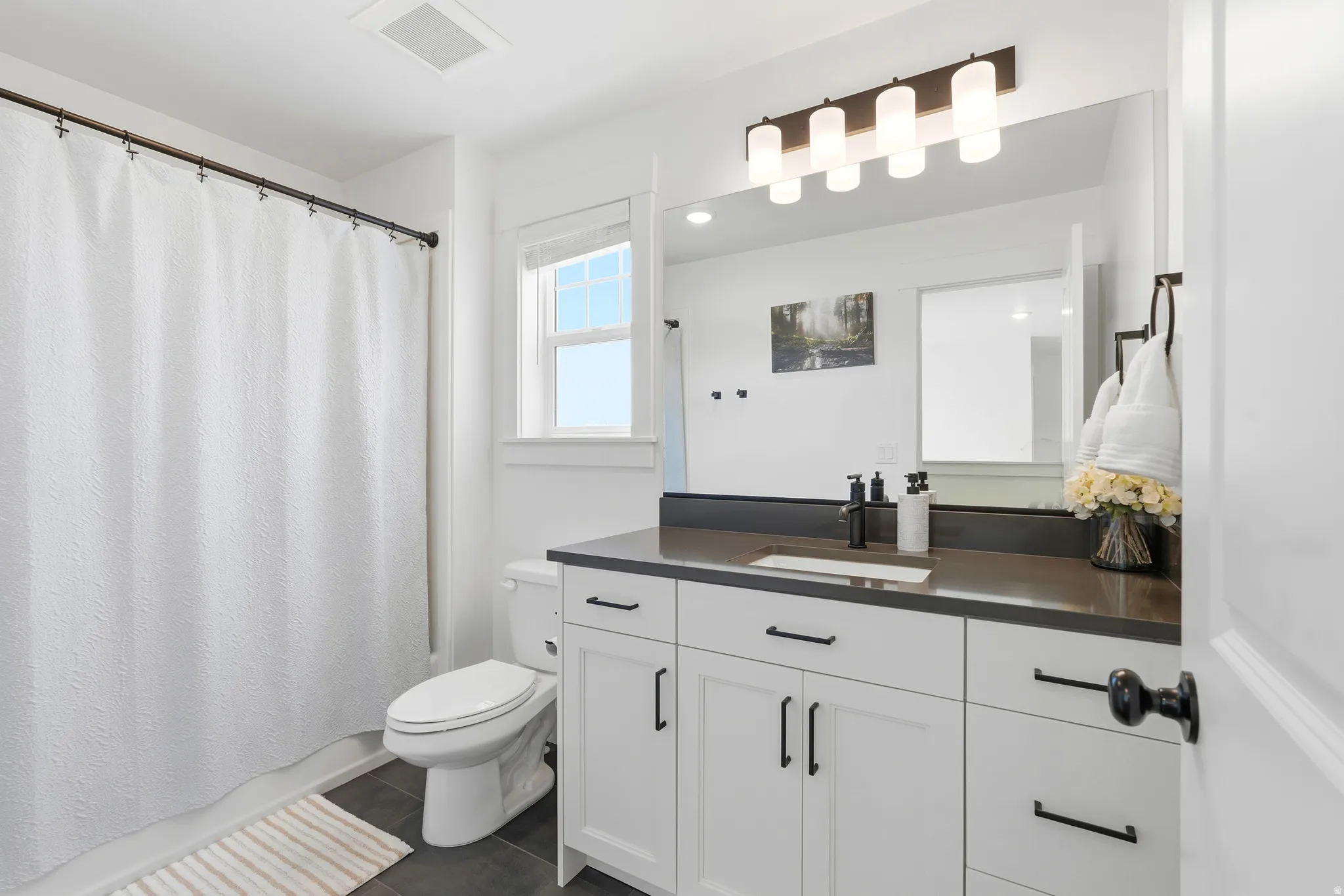 Bathroom featuring a white vanity with dark countertop, an integrated sink, and matte black hardware