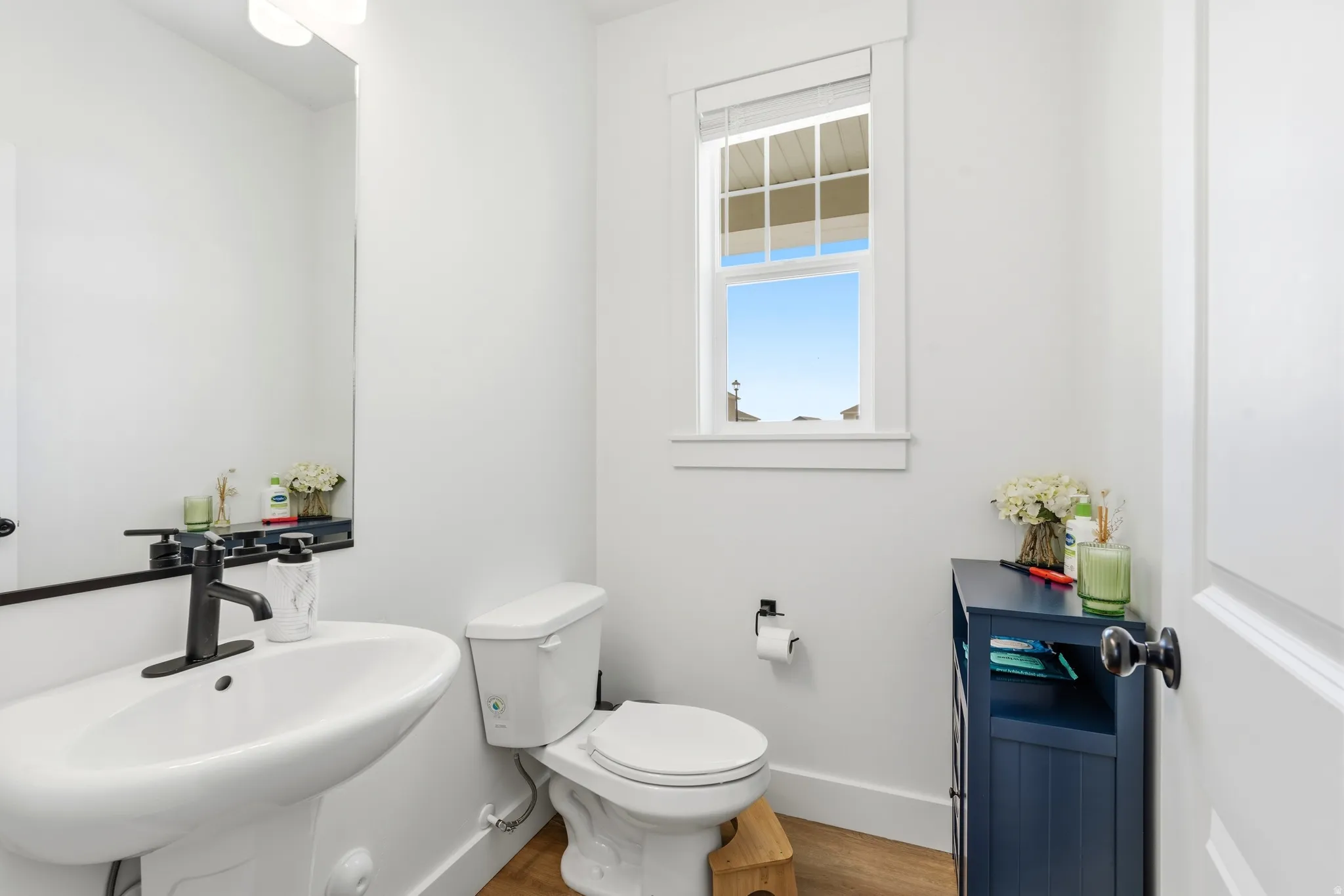 White pedestal sink with matte black faucet, wall-mounted mirror, and white wall sconce lighting