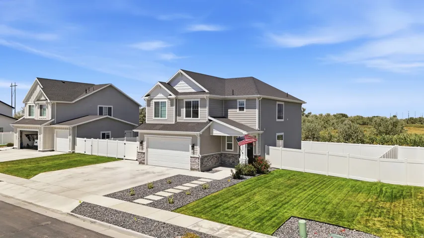 Modern two-story home featuring gray siding with stone accents, a two-car garage, concrete driveway, and a manicured lawn